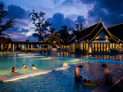 A resort pool with guest swimming in a sunset sky view